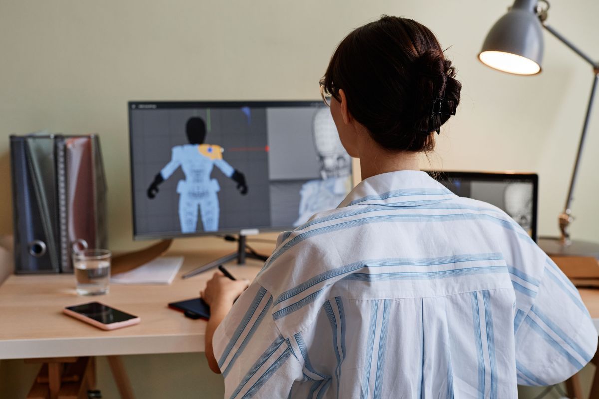 Professional woman working on 3D animation or graphic design at her desk, computer screen displaying a human figure model