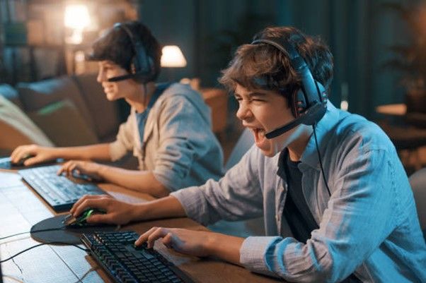 Two gamers engaged in an online gaming session, using headsets and keyboards in a dimly lit environment.
